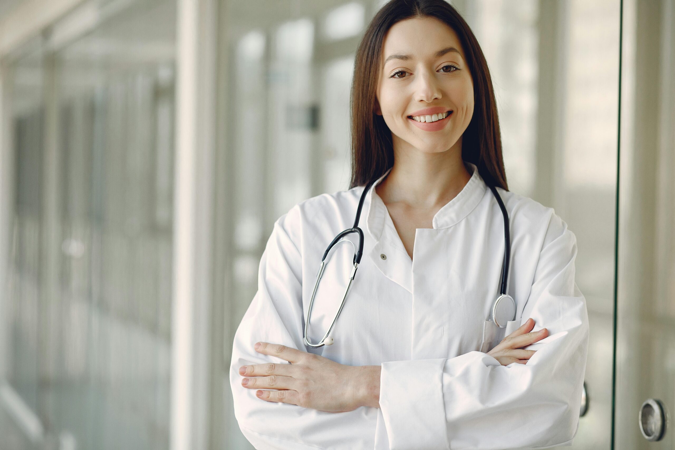 Portrait of a smiling female doctor with arms crossed and stethoscope in a hospital corridor.